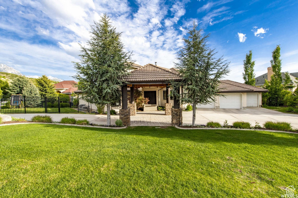 View of front of house featuring driveway, a front yard, a tile roof, and fence