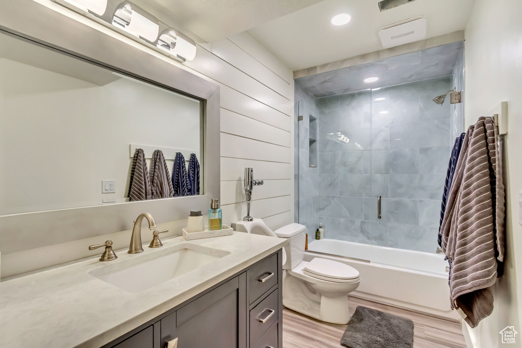 Full bathroom with toilet, vanity, wood finished floors, wood walls, and shower / bath combination