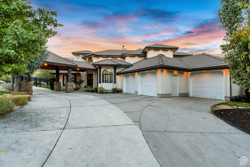 View of front of property with a tiled roof, driveway, stucco siding, and an attached garage