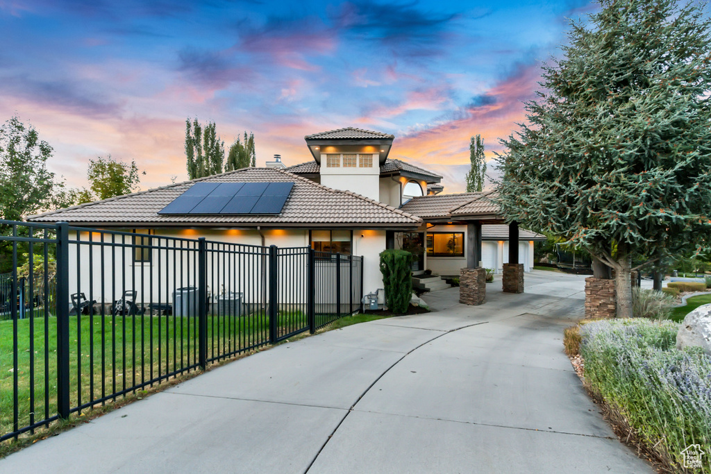 View of front facade with stucco siding, a tiled roof, driveway, a fenced front yard, and solar panels