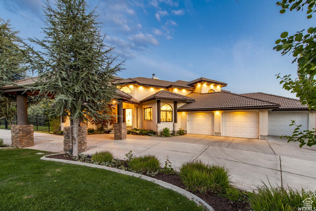 View of front of home with a tile roof, curved driveway, stucco siding, a front lawn, and a garage