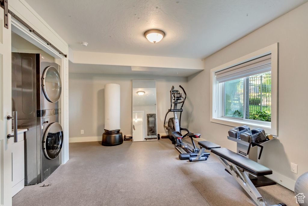 Exercise area featuring baseboards, stacked washing maching and dryer, and a textured ceiling