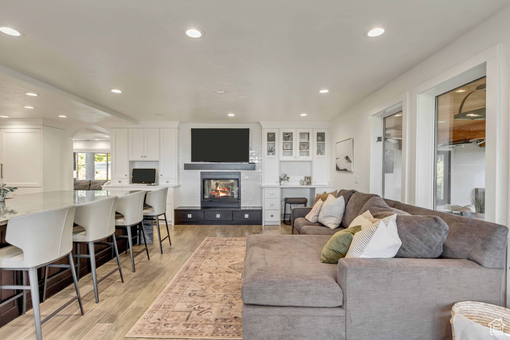 Living area with arched walkways, a fireplace, light wood-style flooring, and recessed lighting