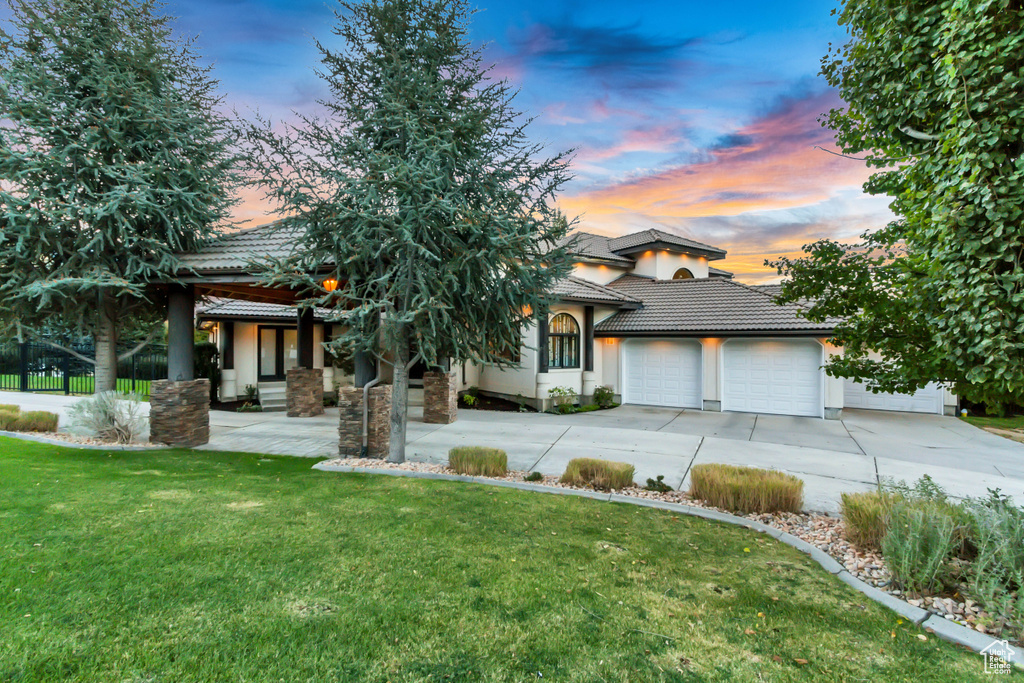 View of front of property featuring a tile roof, driveway, a garage, and a yard