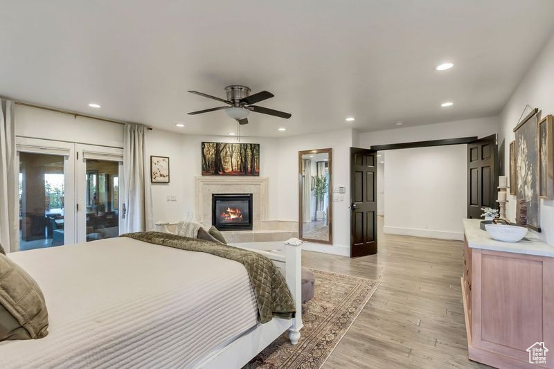 Bedroom featuring light wood finished floors, access to outside, recessed lighting, a glass covered fireplace, and french doors