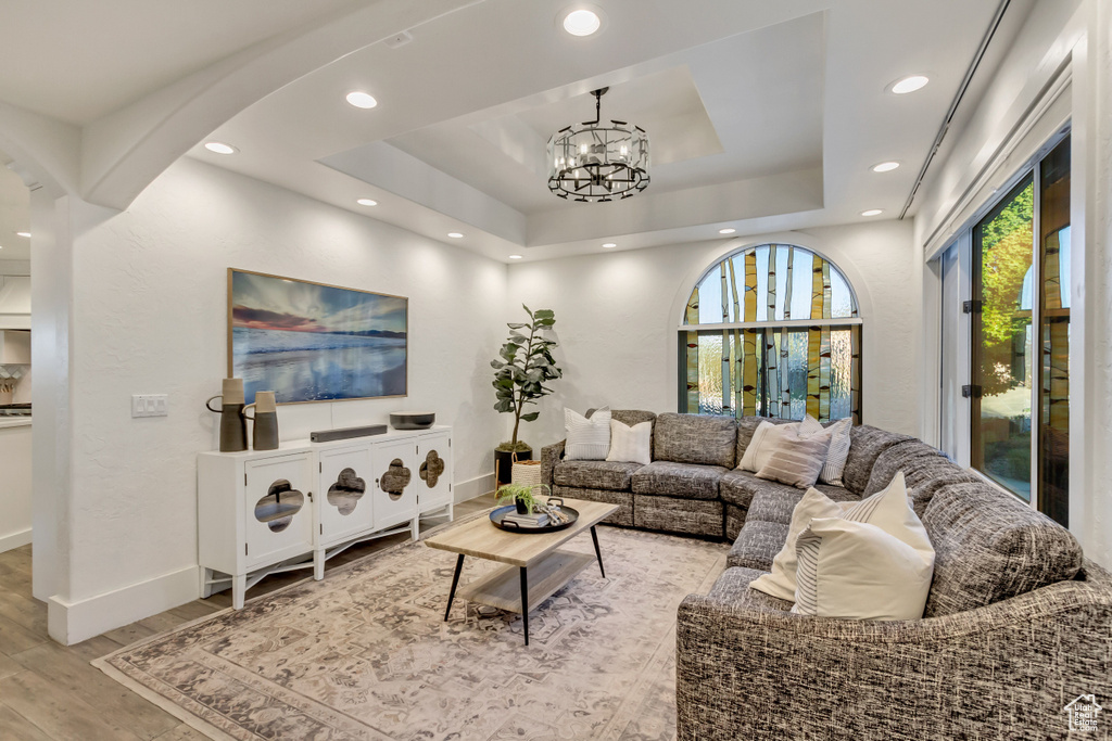 Living area with light wood-style floors, a chandelier, a raised ceiling, baseboards, and arched walkways