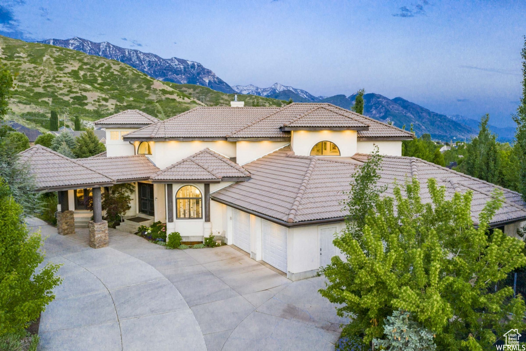 Mediterranean / spanish house featuring an attached garage, a chimney, concrete driveway, a tile roof, and a mountain view