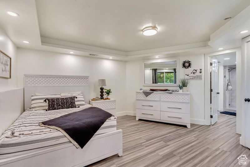 Bedroom with a tray ceiling, baseboards, light wood-type flooring, and recessed lighting