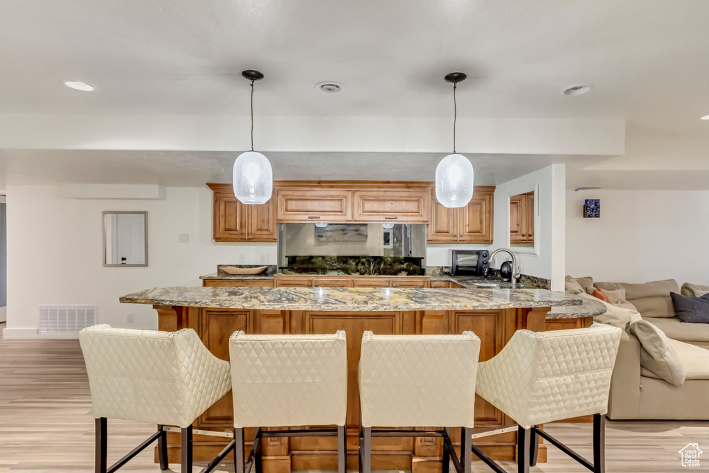 Kitchen featuring visible vents, light stone countertops, a sink, light wood-style floors, and a kitchen breakfast bar
