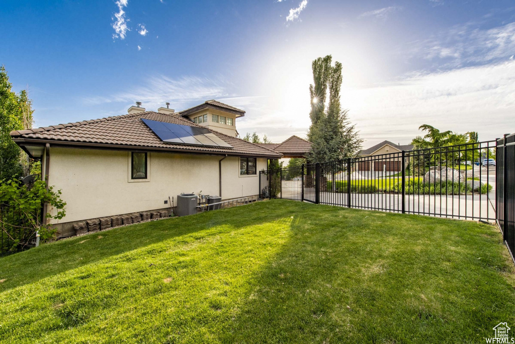 Rear view of house featuring central air condition unit, a lawn, solar panels, and fence
