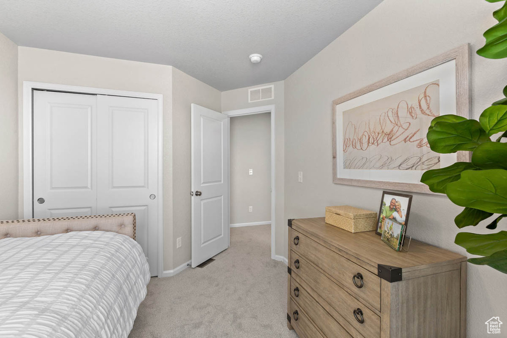 Bedroom with a closet, baseboards, visible vents, and light colored carpet