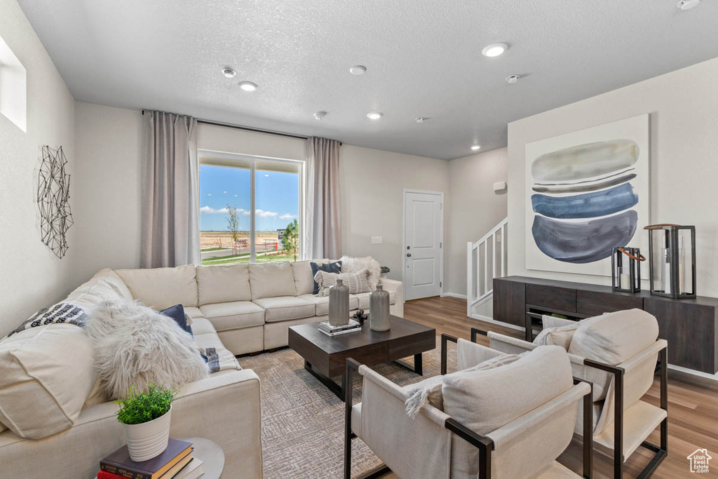 Living room with stairs, recessed lighting, light wood-type flooring, baseboards, and a textured ceiling