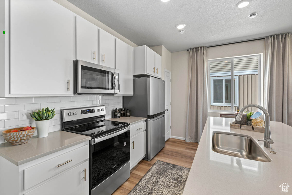 Kitchen with white cabinets, light wood-style flooring, stainless steel appliances, tasteful backsplash, and a sink