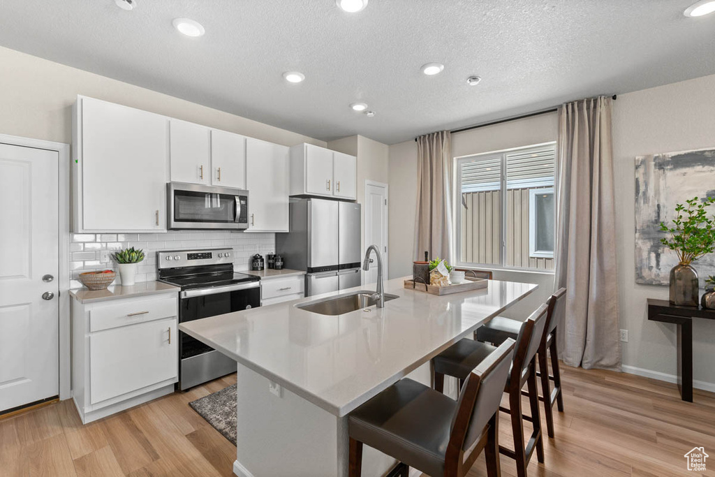 Kitchen featuring a kitchen breakfast bar, light countertops, tasteful backsplash, stainless steel appliances, and a sink