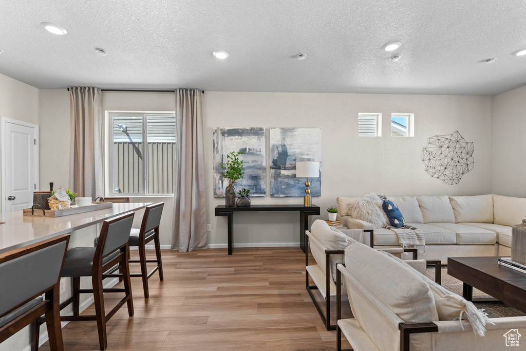 Living area with light wood finished floors, baseboards, recessed lighting, and a textured ceiling