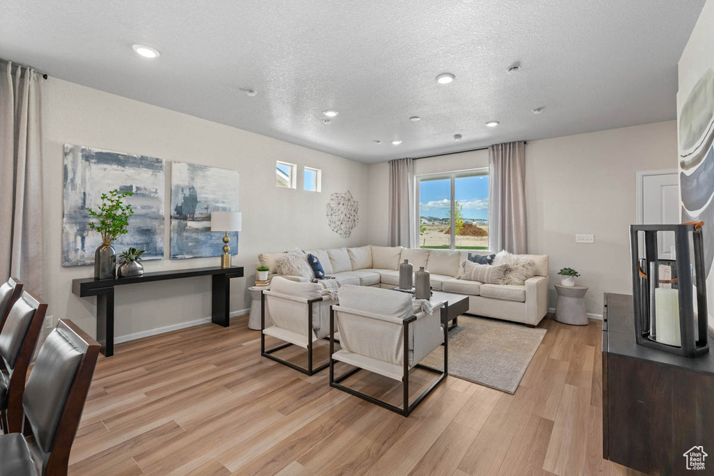 Living area with light wood finished floors, baseboards, recessed lighting, and a textured ceiling