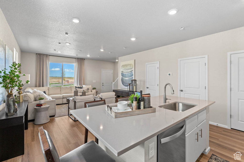 Kitchen with light wood-style flooring, dishwasher, a center island with sink, white cabinetry, and a sink