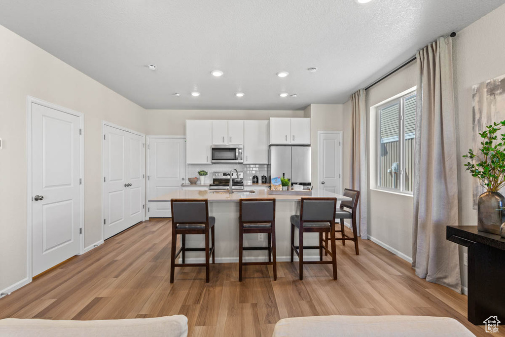 Kitchen featuring a sink, a breakfast bar, stainless steel appliances, a kitchen island with sink, and white cabinets