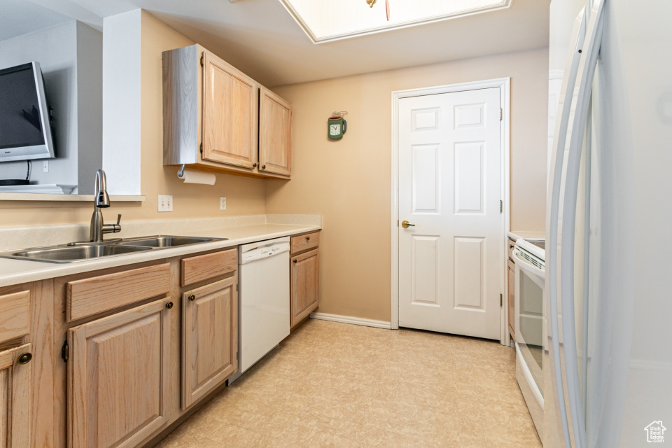 Kitchen featuring light countertops, a sink, light floors, light brown cabinets, and white appliances