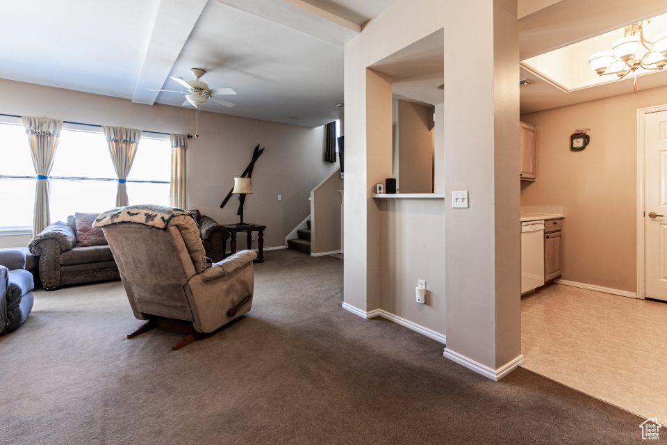 Living room featuring baseboards, carpet flooring, stairs, and ceiling fan with notable chandelier