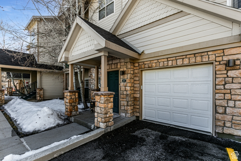 View of front of home featuring stone siding, a porch, driveway, and a garage