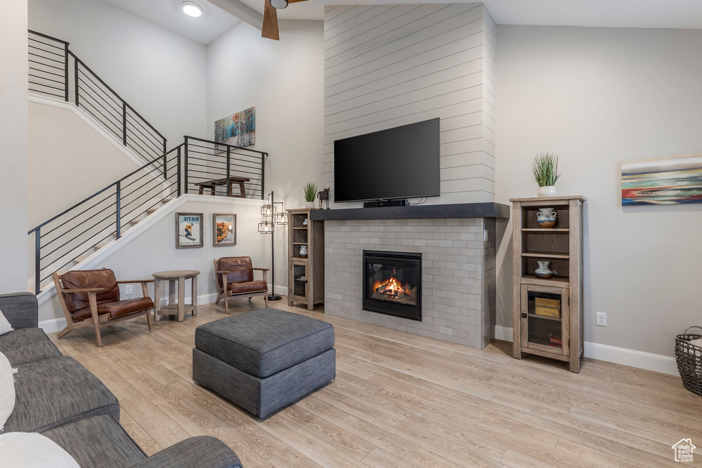 Living area featuring high vaulted ceiling, a glass covered fireplace, wood finished floors, stairway, and baseboards