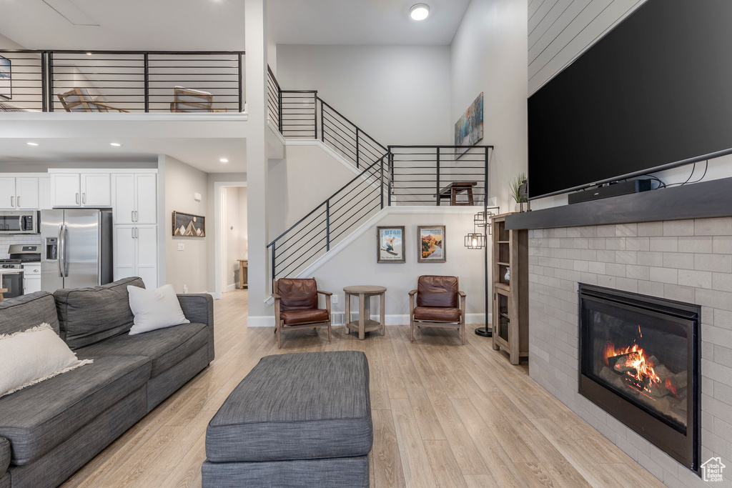 Living room featuring a fireplace, light wood finished floors, stairway, a high ceiling, and baseboards