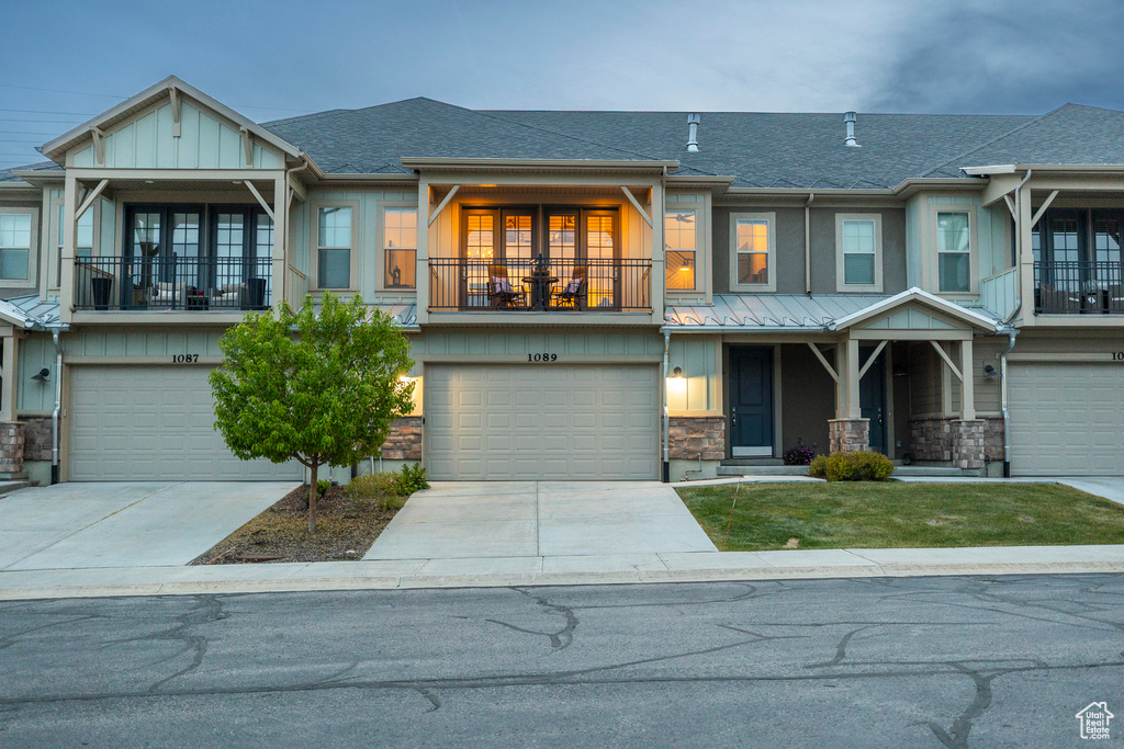 View of front of home featuring a balcony, stone siding, a shingled roof, an attached garage, and board and batten siding