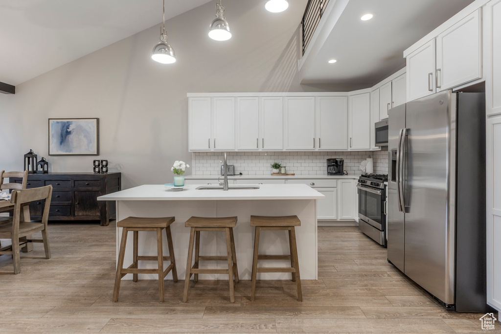 Kitchen with stainless steel appliances, a sink, decorative backsplash, a breakfast bar area, and high vaulted ceiling