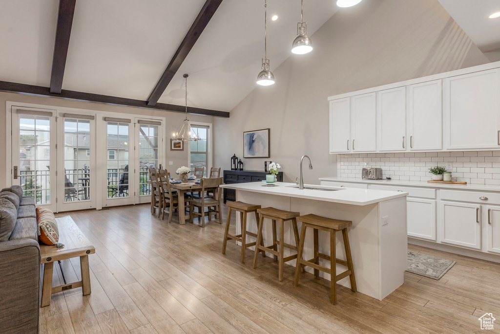 Kitchen featuring a sink, backsplash, light wood-style floors, light countertops, and beamed ceiling