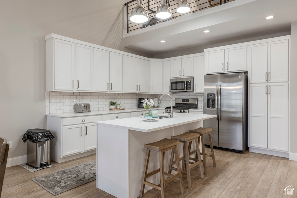 Kitchen with appliances with stainless steel finishes, light countertops, decorative backsplash, light wood finished floors, and recessed lighting