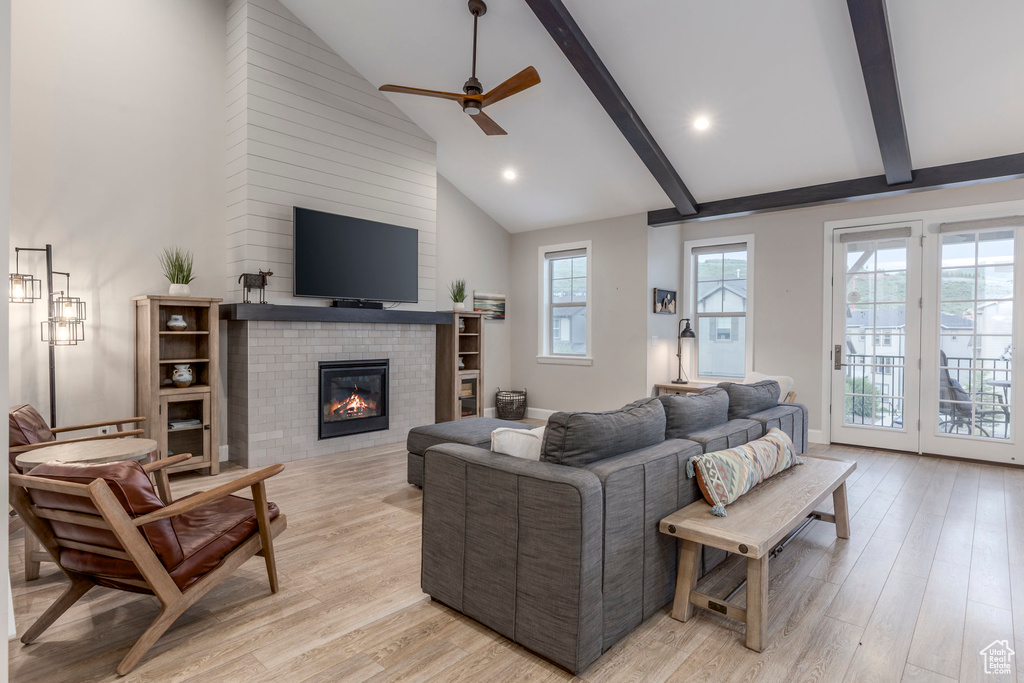 Living area with ceiling fan, beam ceiling, light wood-style floors, a fireplace, and high vaulted ceiling
