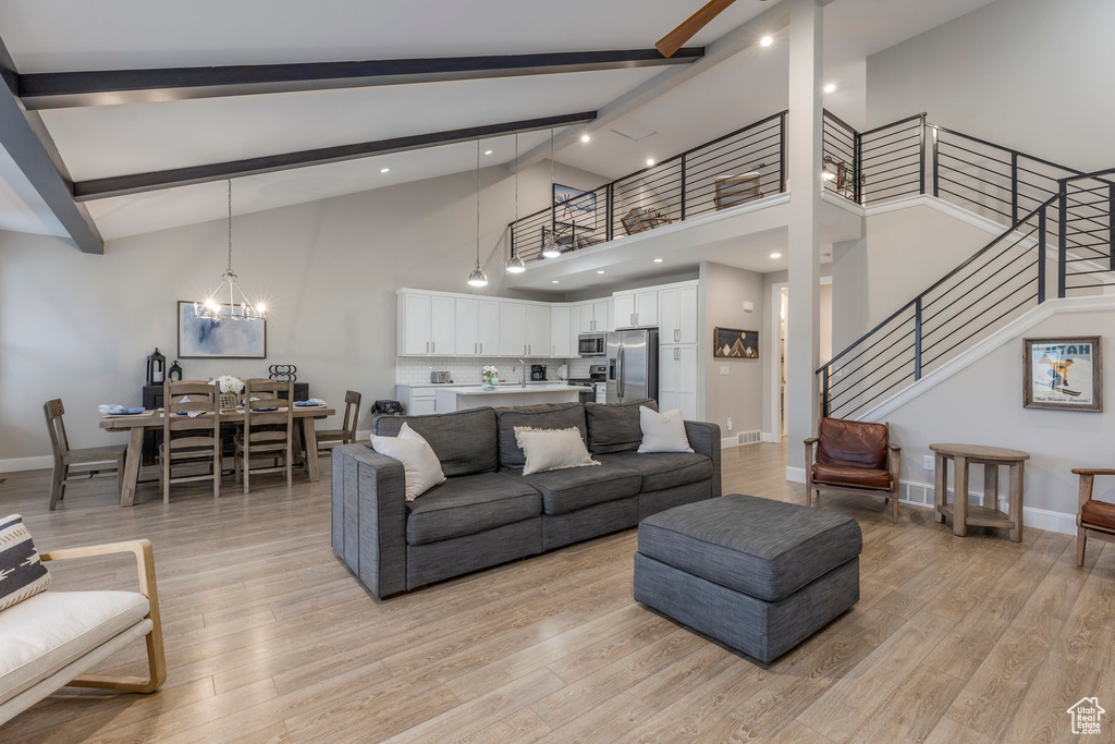 Living room with beam ceiling, stairway, light wood-type flooring, baseboards, and high vaulted ceiling