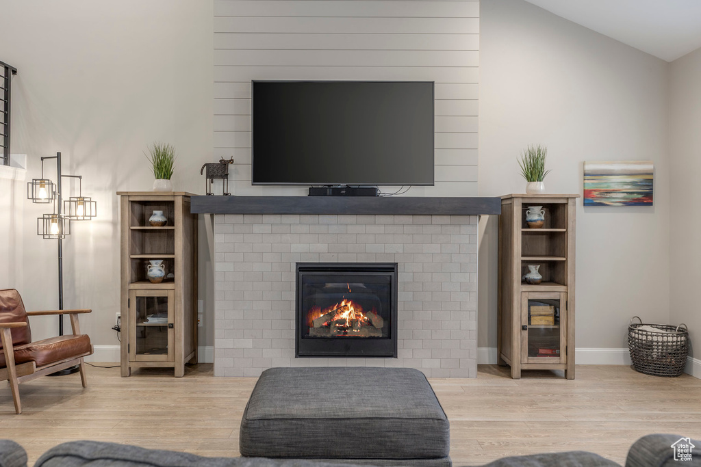 Living area featuring wood finished floors, a brick fireplace, baseboards, and lofted ceiling