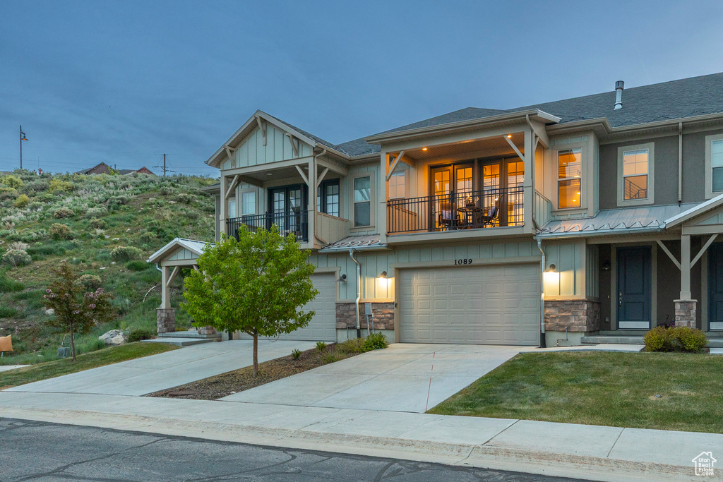 Townhome / multi-family property with a balcony, board and batten siding, stone siding, and a garage