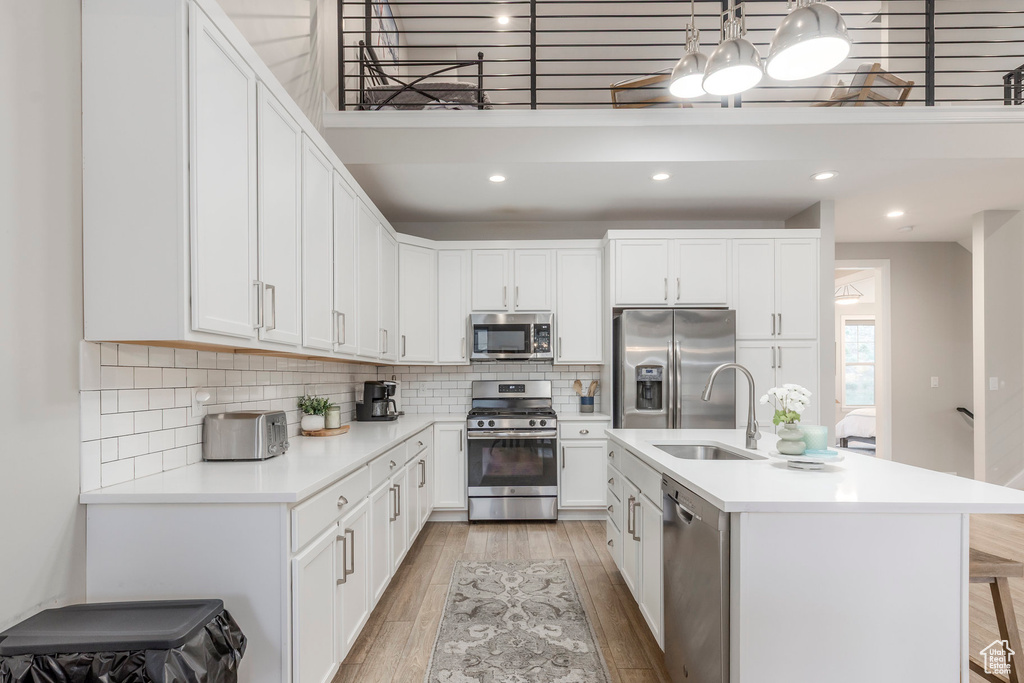 Kitchen with appliances with stainless steel finishes, a sink, light wood-style flooring, light countertops, and decorative backsplash