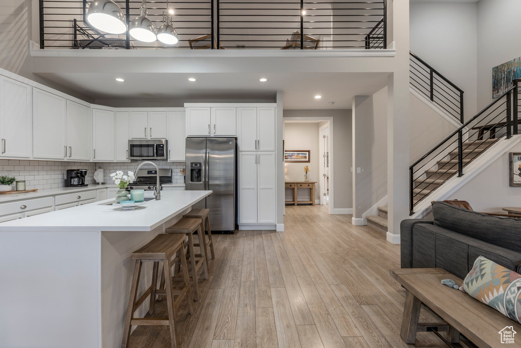 Kitchen with stainless steel appliances, a high ceiling, light wood-style floors, light countertops, and white cabinetry