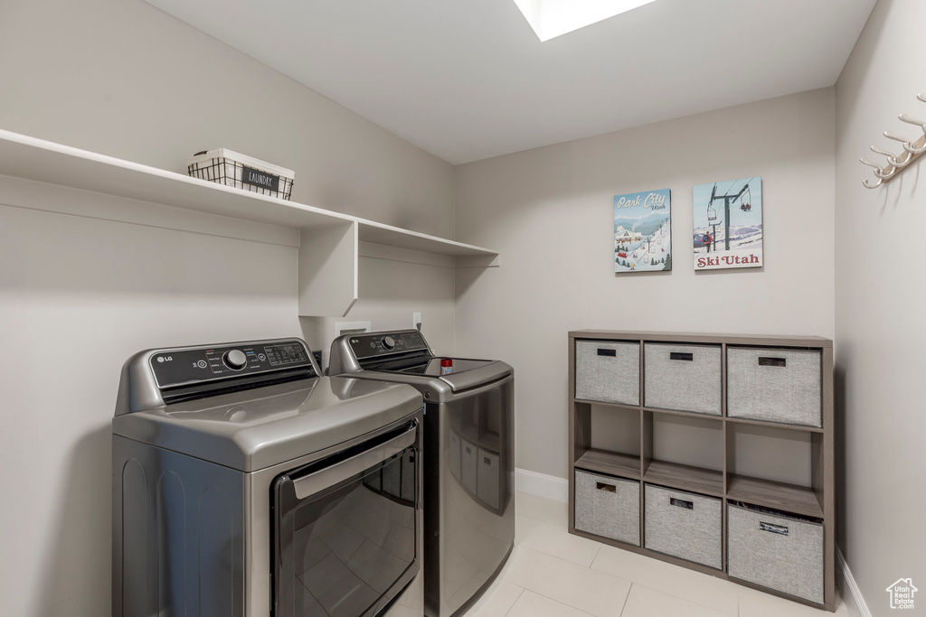 Washroom with washing machine and dryer, light tile patterned flooring, and baseboards