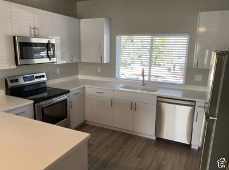 Kitchen featuring light countertops, dark wood-style flooring, a sink, white cabinets, and appliances with stainless steel finishes