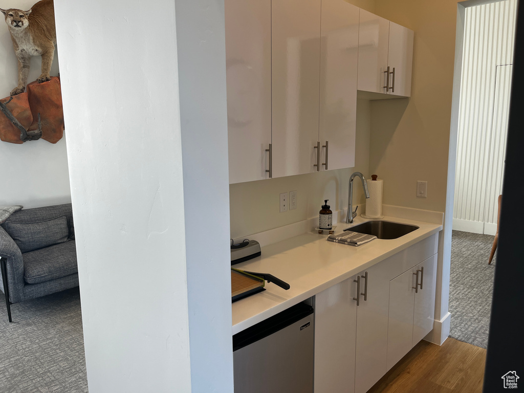 Kitchen with light countertops, a sink, white cabinets, dishwashing machine, and wood finished floors