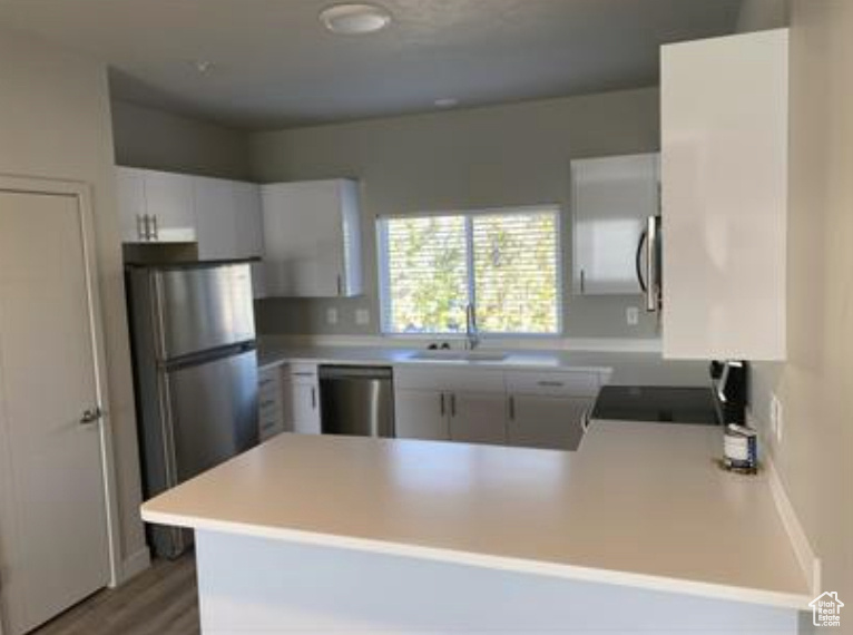 Kitchen featuring light countertops, light wood-type flooring, a sink, a peninsula, and appliances with stainless steel finishes