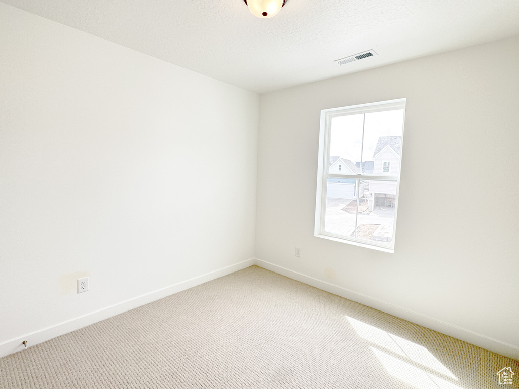 Empty room with light carpet, a textured ceiling, baseboards, and visible vents
