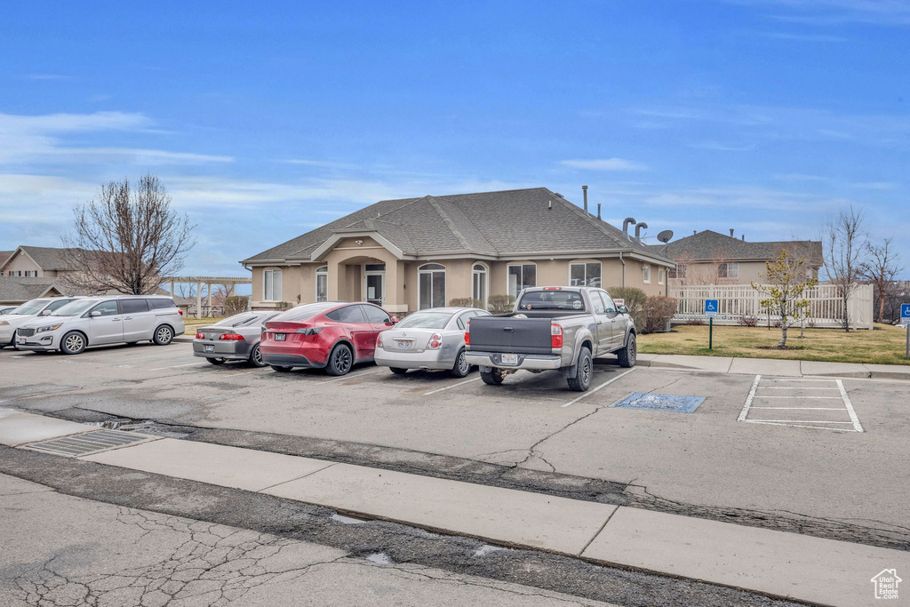 View of front of property featuring stucco siding, a shingled roof, uncovered parking, and fence