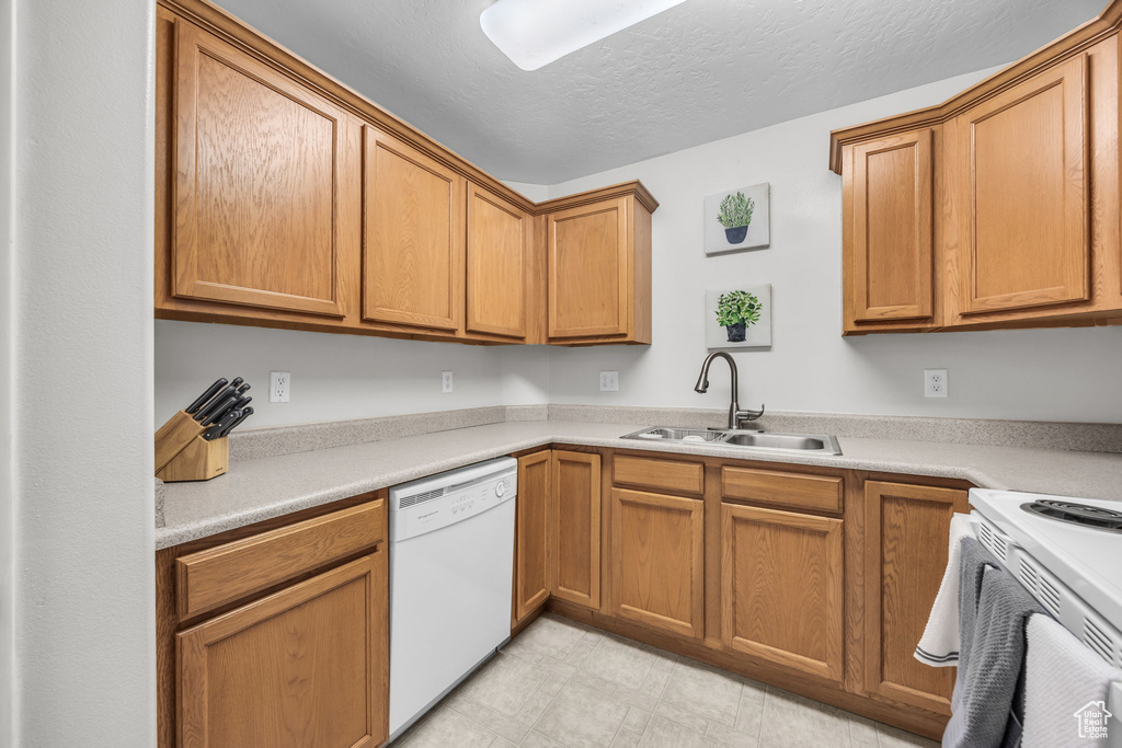 Kitchen with light countertops, white appliances, a textured ceiling, a sink, and light floors