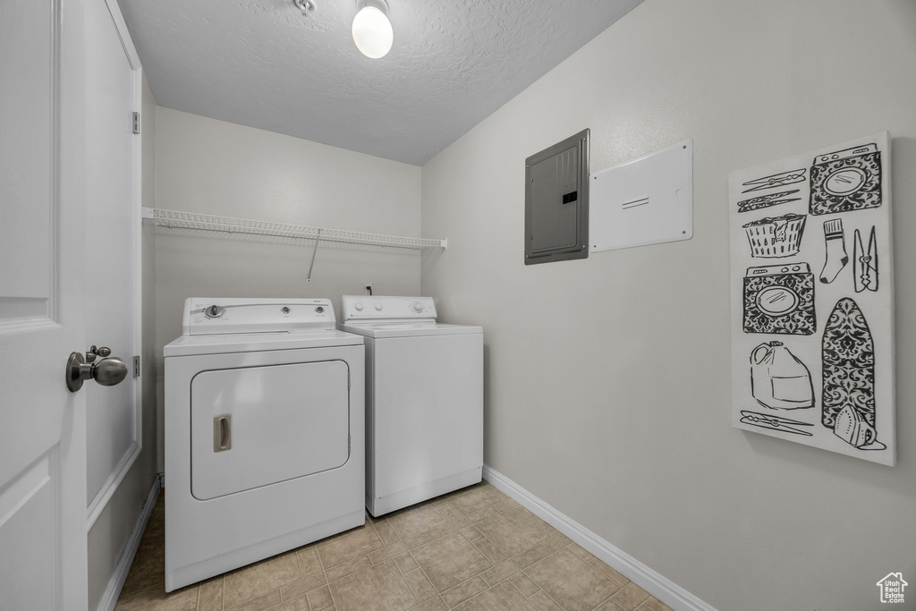 Washroom featuring electric panel, a textured ceiling, laundry area, baseboards, and washer and dryer
