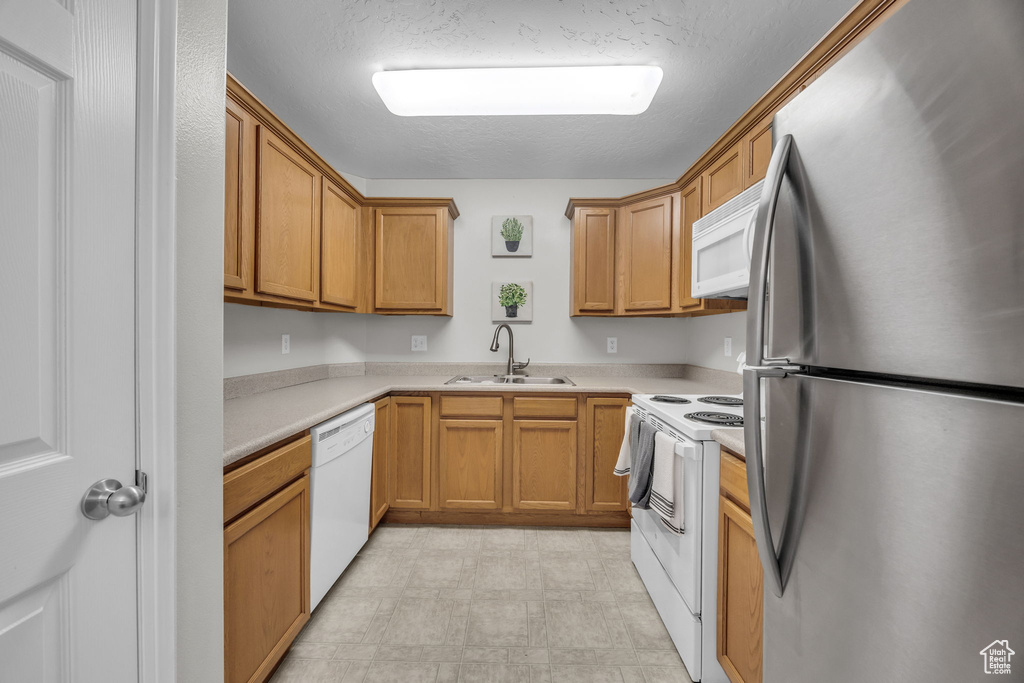 Kitchen with a textured ceiling, light countertops, white appliances, light floors, and a sink