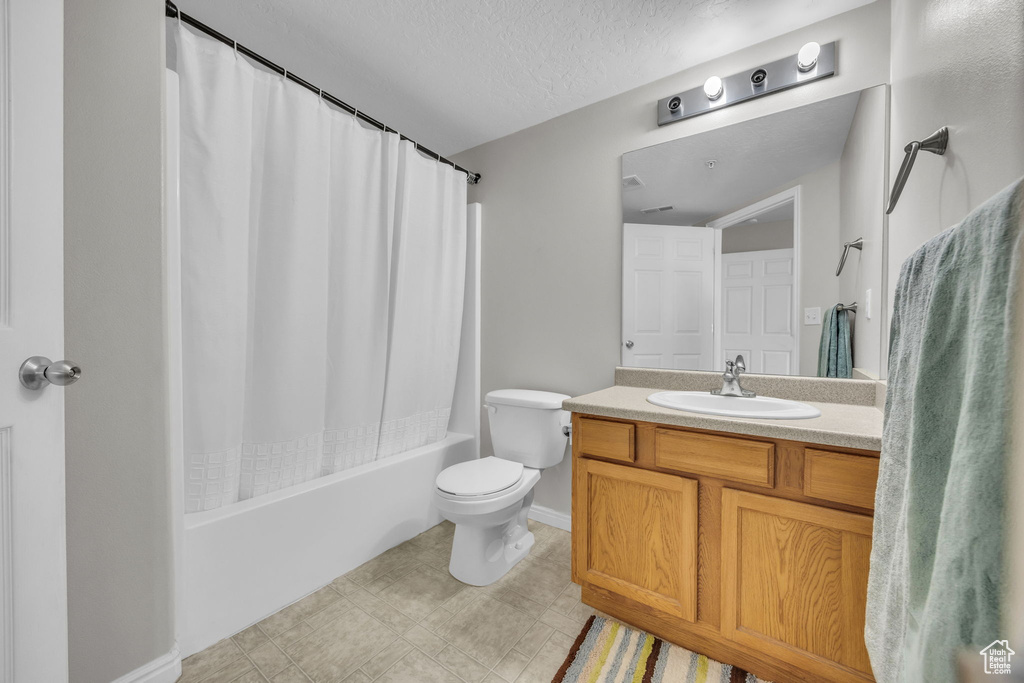 Full bathroom featuring a textured ceiling, baseboards, toilet, vanity, and shower / tub combo with curtain