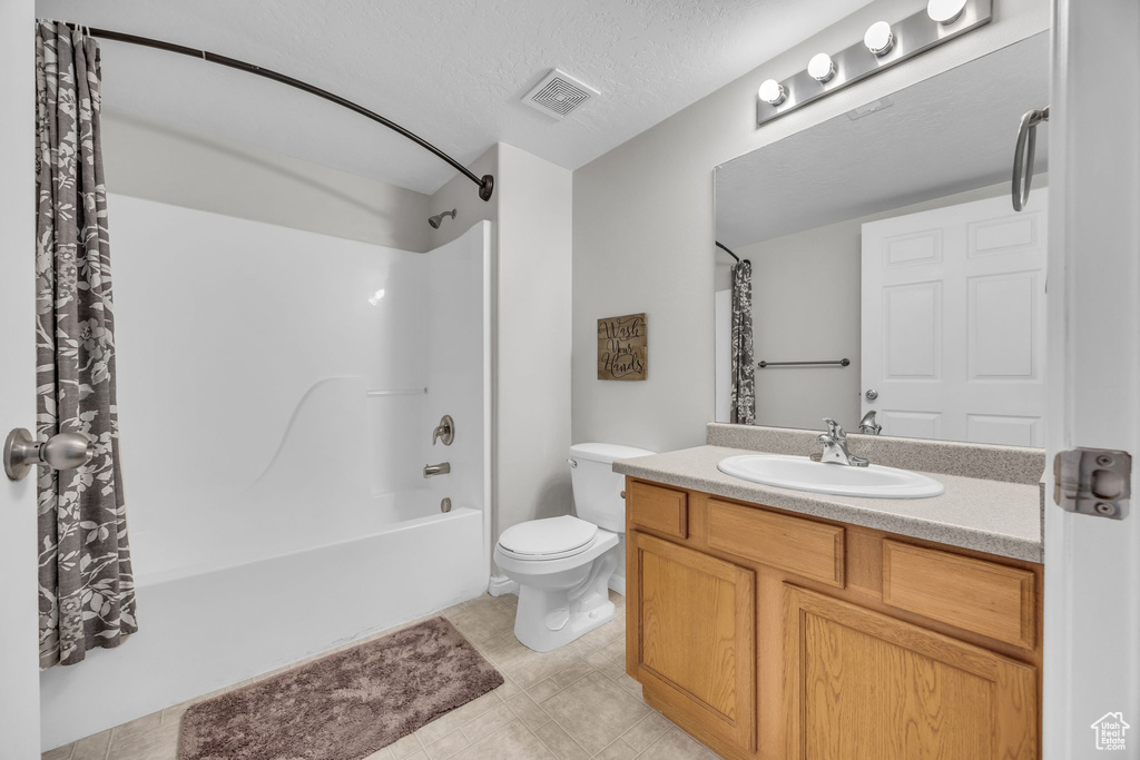 Bathroom with a textured ceiling, visible vents, toilet, vanity, and shower / bath combination with curtain