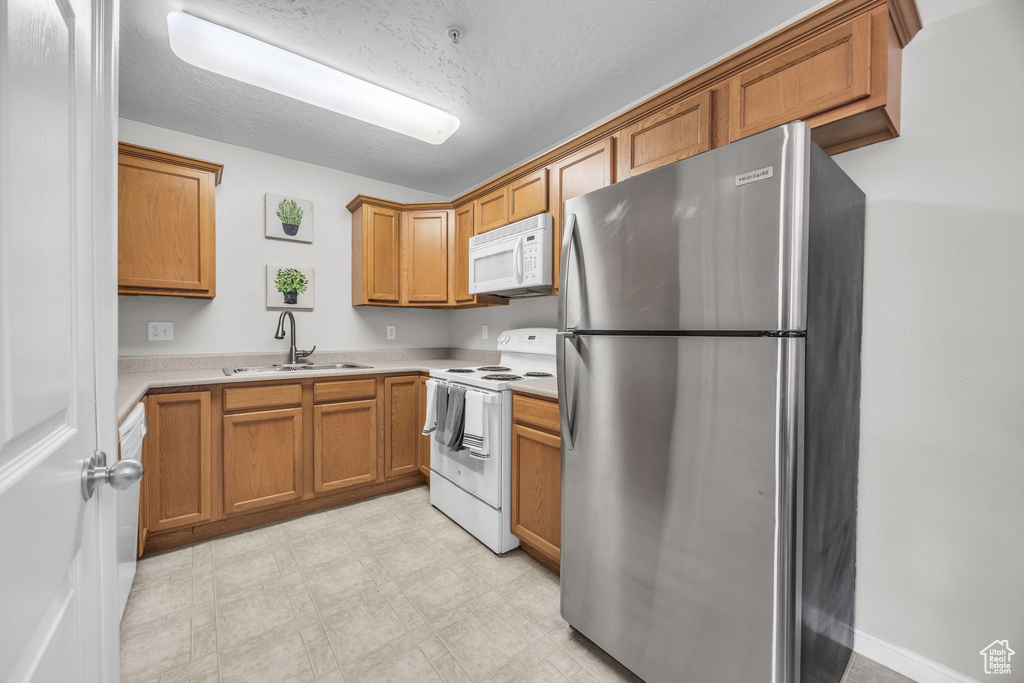Kitchen with light countertops, a sink, light floors, brown cabinetry, and white appliances