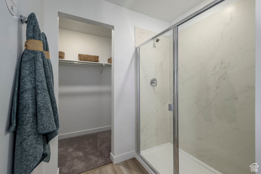 Bathroom featuring a spacious closet, a marble finish shower, baseboards, and wood finished floors